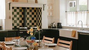 Una cucina con piastrelle a scacchi, un tavolo da pranzo apparecchiato con piatti e bicchieri, e una finestra con tende.
