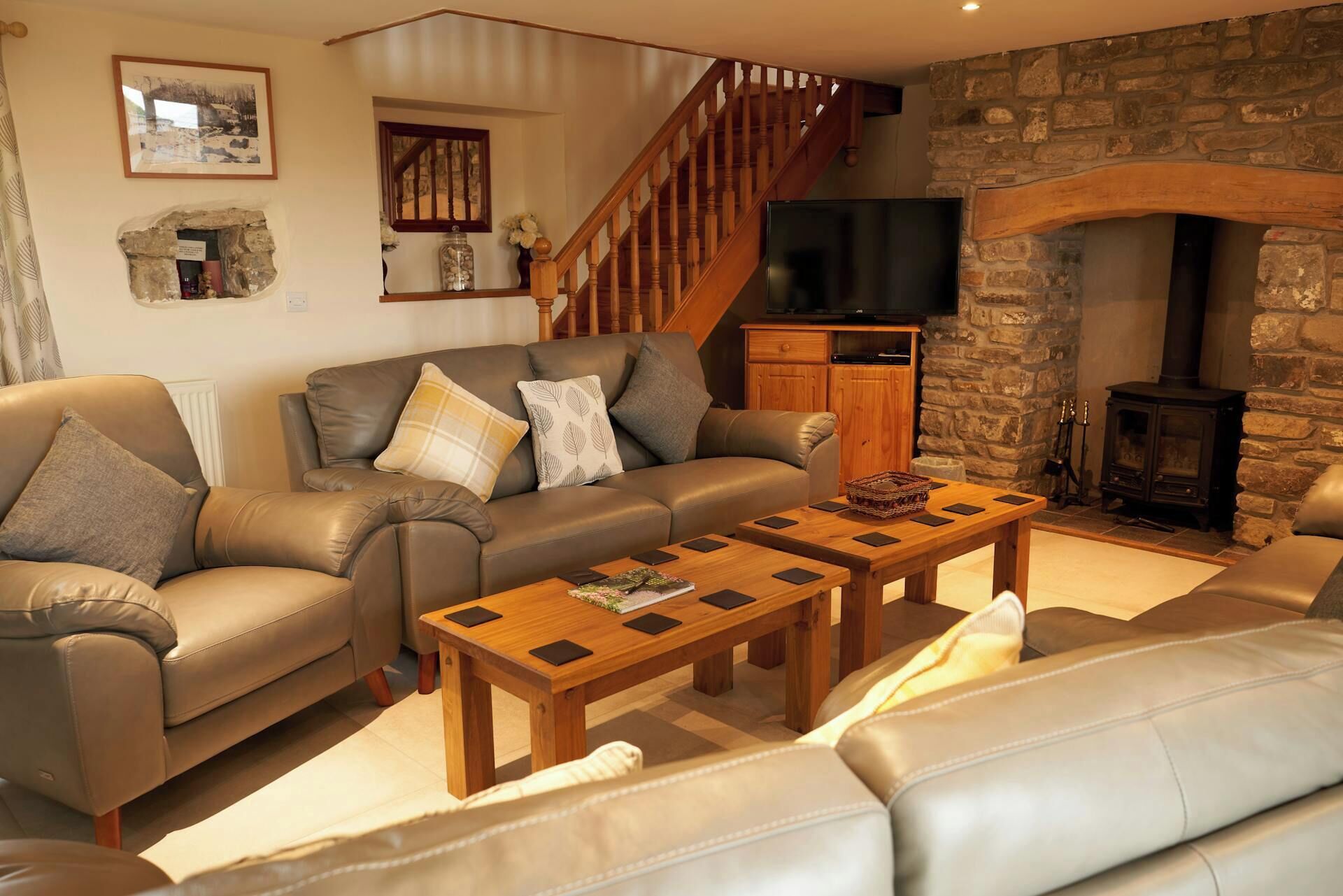 A living room with a stone fireplace, a wooden staircase, a leather sofa, and a television.