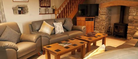A living room with a stone fireplace, a wooden staircase, a leather sofa, and a television.