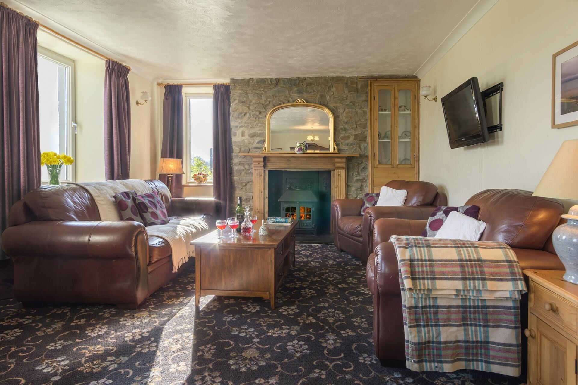 A cozy living room with leather sofas, a wooden coffee table, a stone fireplace, and a television on the wall.