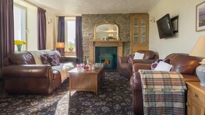 Una sala de estar acogedora con sofás de cuero, una mesa de centro de madera, una chimenea de piedra y un televisor en la pared.