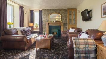 A cozy living room with leather sofas, a wooden coffee table, a stone fireplace, and a television on the wall.