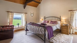 Un dormitorio con cama, mesitas de noche, una silla y vistas al exterior.