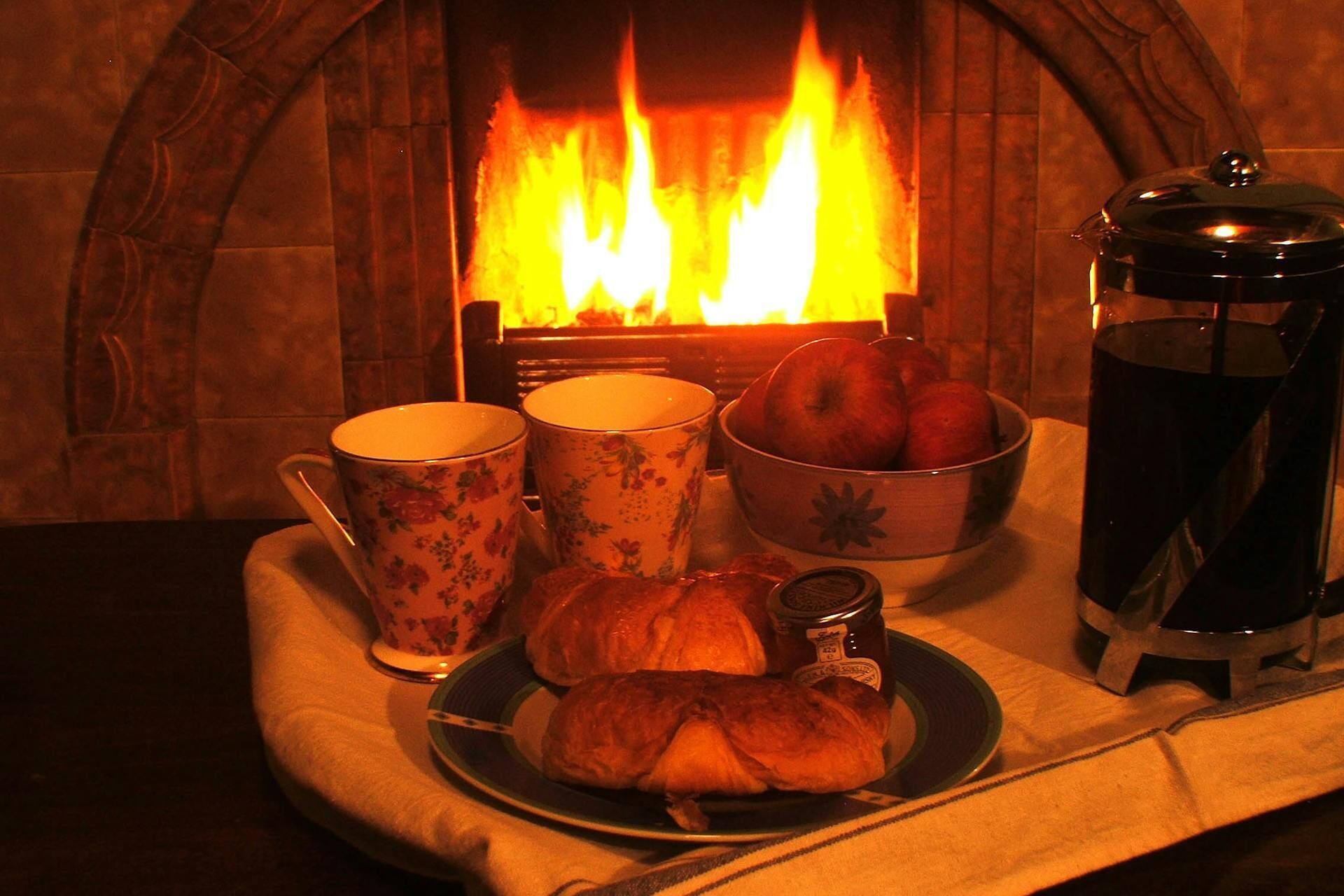 Un cadre chaleureux avec une cheminée, un plateau contenant des croissants, des pommes et une cafetière.