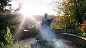 A statue of a woman reading a book, surrounded by a stone wall and greenery. - 2 Castle Hall, Llangrannog (Llangrannog)