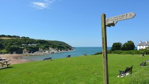 A wooden signpost with directional information, a grassy area with benches, and a view of a beach and sea. - Arwel, Aberporth - Three Bedroom Cottage, Sleeps 6 (Aberporth)