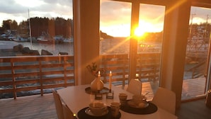 A dining table with a candle centerpiece, a view of the sunset over water, and a wooden deck.