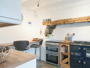 Een keuken met een houten aanrecht, twee zwarte ovens, een fornuis, een stenen muur en een hangende lamp.