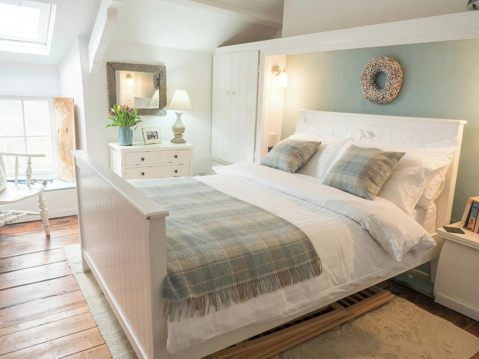 A bedroom with a bed, bedside tables, a nightstand, a mirror, a window, and a wall-mounted light fixture.
