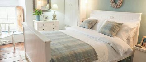 A bedroom with a bed, bedside tables, a nightstand, a mirror, a window, and a wall-mounted light fixture.