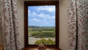 Ein Fenster mit Blick auf eine ländliche Landschaft, ein Holztisch mit Teekanne und gemusterte Vorhänge.