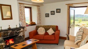Ein gemütliches Wohnzimmer mit Kamin aus Stein, einer Couch, einem Couchtisch aus Holz und Blick ins Freie durch eine Schiebetür.