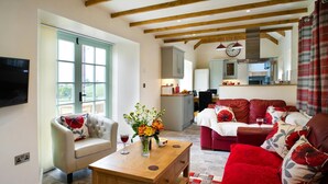 Una sala de estar con sofá, sillón, mesa de centro y televisor. Se observa una cocina al fondo.