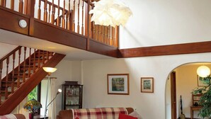 A cozy living room with a wooden staircase, a plaid sofa, and a large window. - Fedwen Uchaf, Tresaith (Tresaith)
