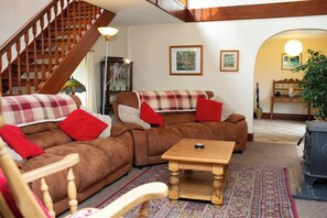 A living room with a brown sofa set, a wooden coffee table, a wooden chair, a staircase, and a lamp.