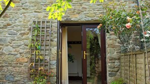 A stone building with a wooden door, a small garden with plants and flowers, and a metal fence. - Fedwen Uchaf, Tresaith (Tresaith)