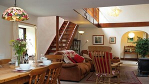 A dining area with a wooden table, chairs, and a vase of flowers. There is a staircase leading to an upper level. - Fedwen Uchaf, Tresaith (Tresaith)