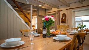 Un coin repas avec une table en bois dressée pour quatre personnes, un vase de fleurs et une bouteille de vin.