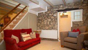 Un salon chaleureux avec un canapé rouge, un canapé beige et un mur en pierre.