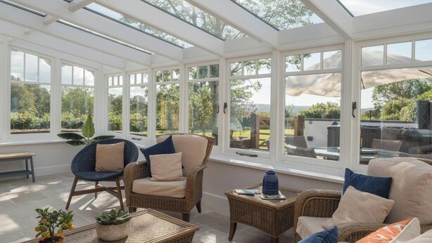 Une véranda meublée de mobilier en osier, agrémentée de plantes en pot et offrant une vue sur le jardin.