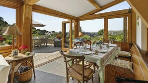 A wooden-framed conservatory with a table set for dining, chairs, and a wicker basket. - Castle Reach, Newport (Newport)