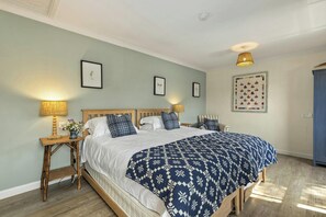 A bedroom with a bed, two bedside tables, a lamp, a wall clock, and a quilted wall hanging.