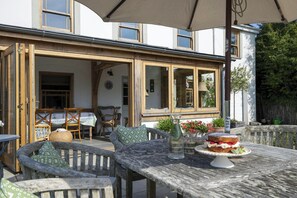 An outdoor dining area with wooden furniture, a table with a cake, and a pergola overhead.