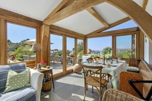 Ein Wintergarten mit Esstisch, einer Couch und Blick ins Grüne.