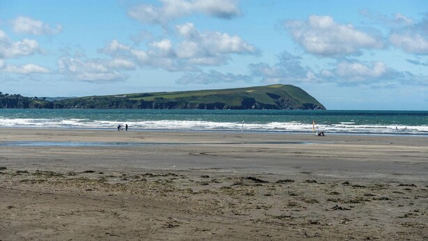 A beach with a distant green hill, waves, and a clear sky. - Castle Reach, Newport (Newport)