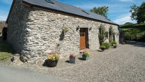 A stone building with a sloped roof, a wooden door, and a gravel driveway. - Eirlys, Aberystwyth - Two Bedroom Cottage, Sleeps 4 (Llanrhystud)