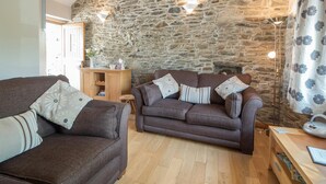 Un salon chaleureux avec un mur en pierre, des poutres en bois, une cheminée et un canapé agrémenté de coussins décoratifs.