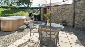 Une terrasse extérieure avec un jacuzzi, une table et des chaises, et un grand parasol.