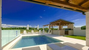 A swimming pool with lounge chairs and a barbecue area under a pergola. - Beautiful Villa Gloria Vita with pool and jacuzzi (Nova Vas)