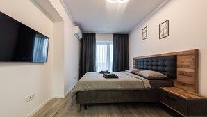 Une chambre à coucher moderne avec un grand lit, un téléviseur fixé au mur et une table de chevet en bois.