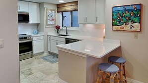 Une cuisine moderne avec des meubles blancs, un îlot central et deux tabourets de bar.