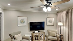 Una sala moderna con ventilador de techo, un televisor de pantalla plana, dos sillones, una mesa de centro y obras de arte enmarcadas en las paredes.