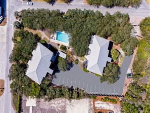 An aerial view of a residential area with two houses, a swimming pool, and a road. - Inlet Dunes #102 | Steps to Beach + Pool! (30A)