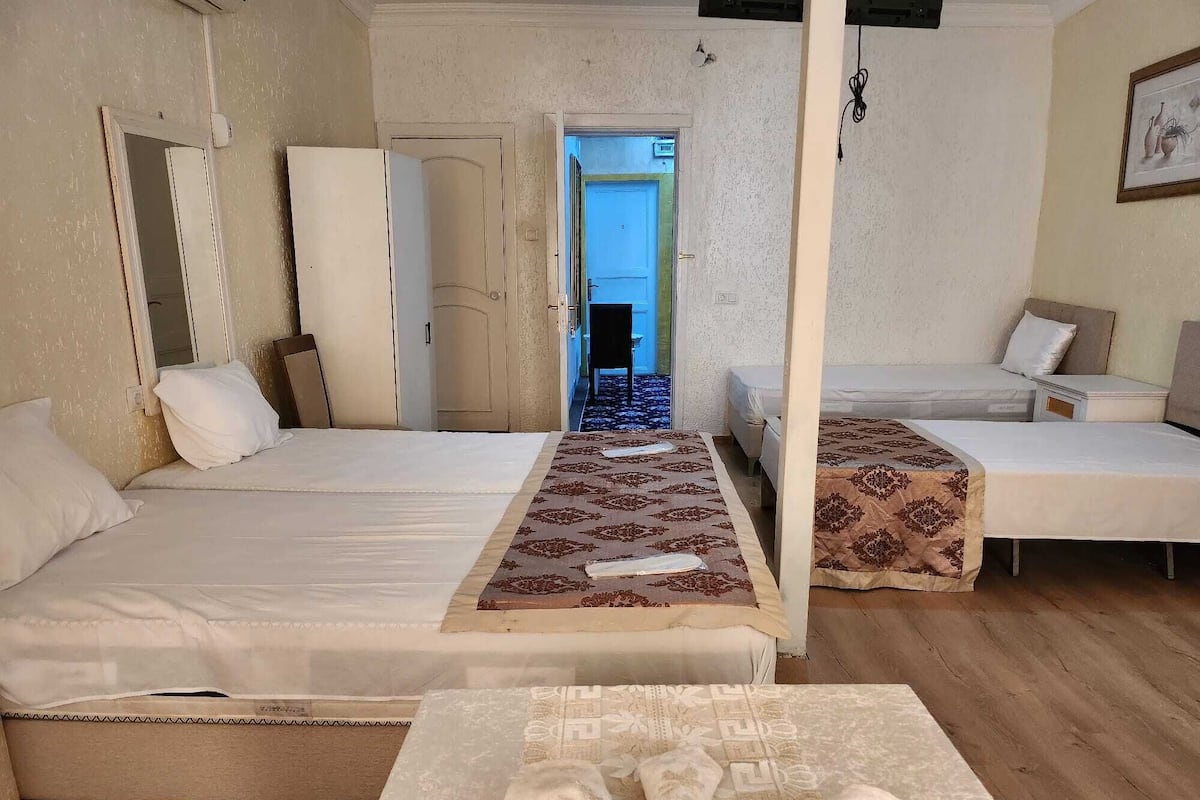 A hotel room with two single beds, a small table with decorative items, and a view of the outside.