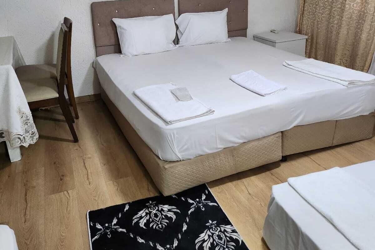 A hotel room with a bed, bedside tables, a chair, a small table, and an air conditioning unit.