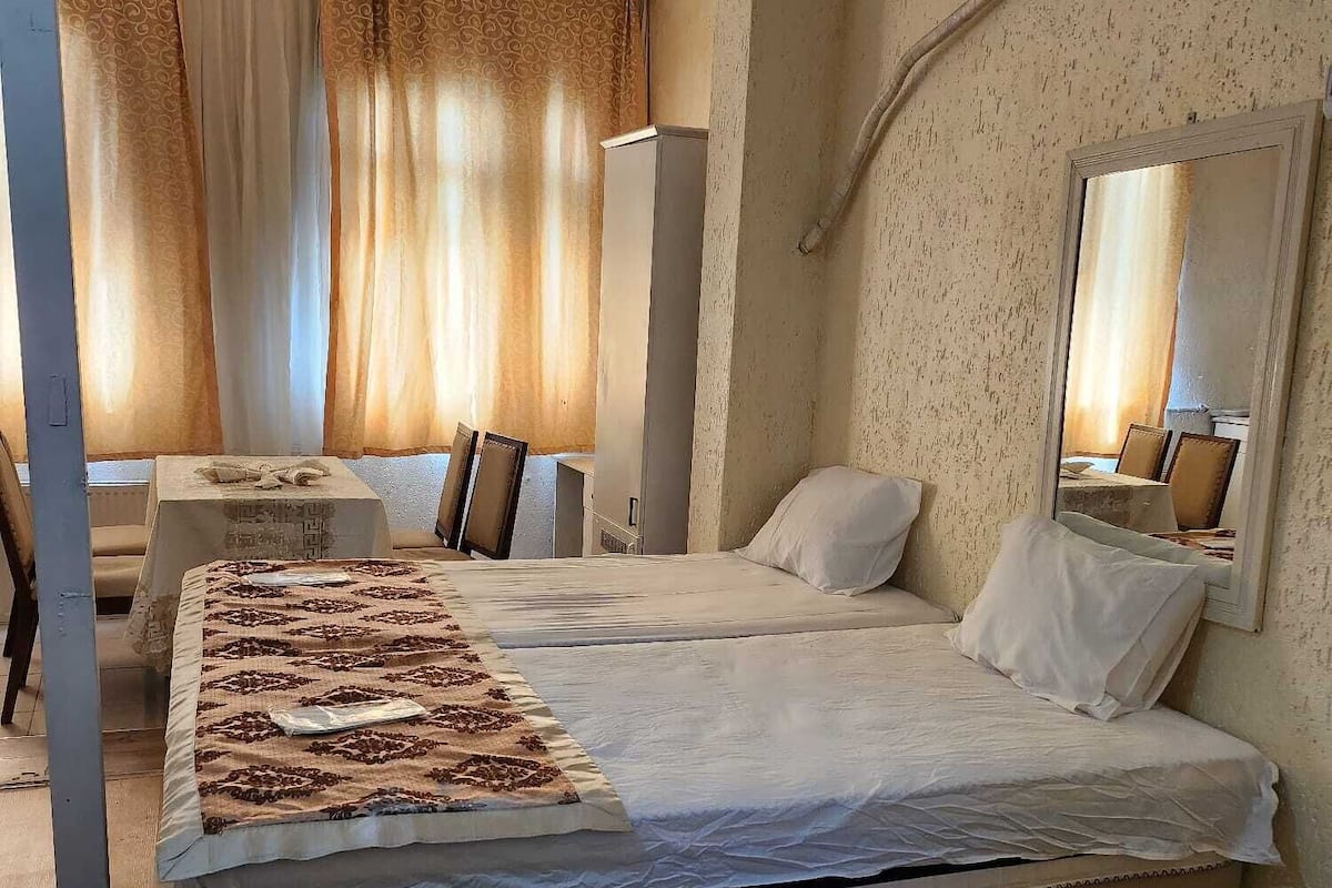 A hotel room with a large bed, a desk, and a chair. There is a mirror on the wall and an air conditioning unit.