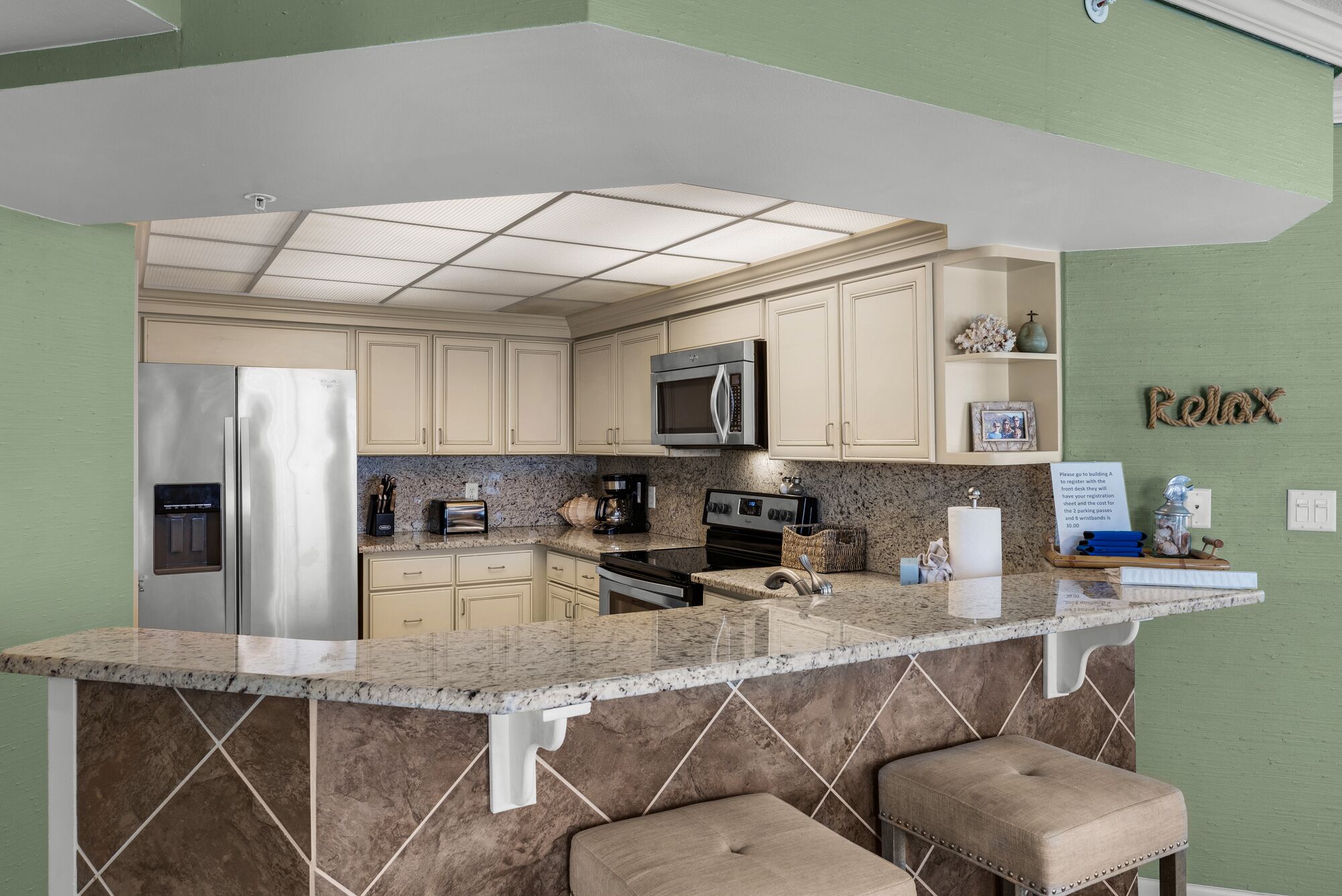 Una cocina con una isla central, electrodomésticos de acero inoxidable y una pared de acento verde.