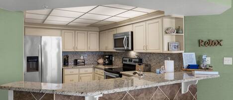 Una cocina con una isla central, electrodomésticos de acero inoxidable y una pared de acento verde.