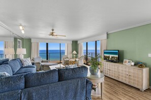 A spacious living room with a large sofa, a television, and a view of the ocean.