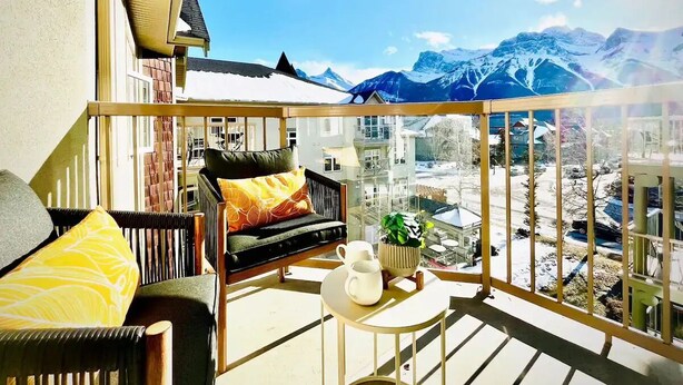 A balcony with a sofa, a small table, and a view of snow-covered mountains.