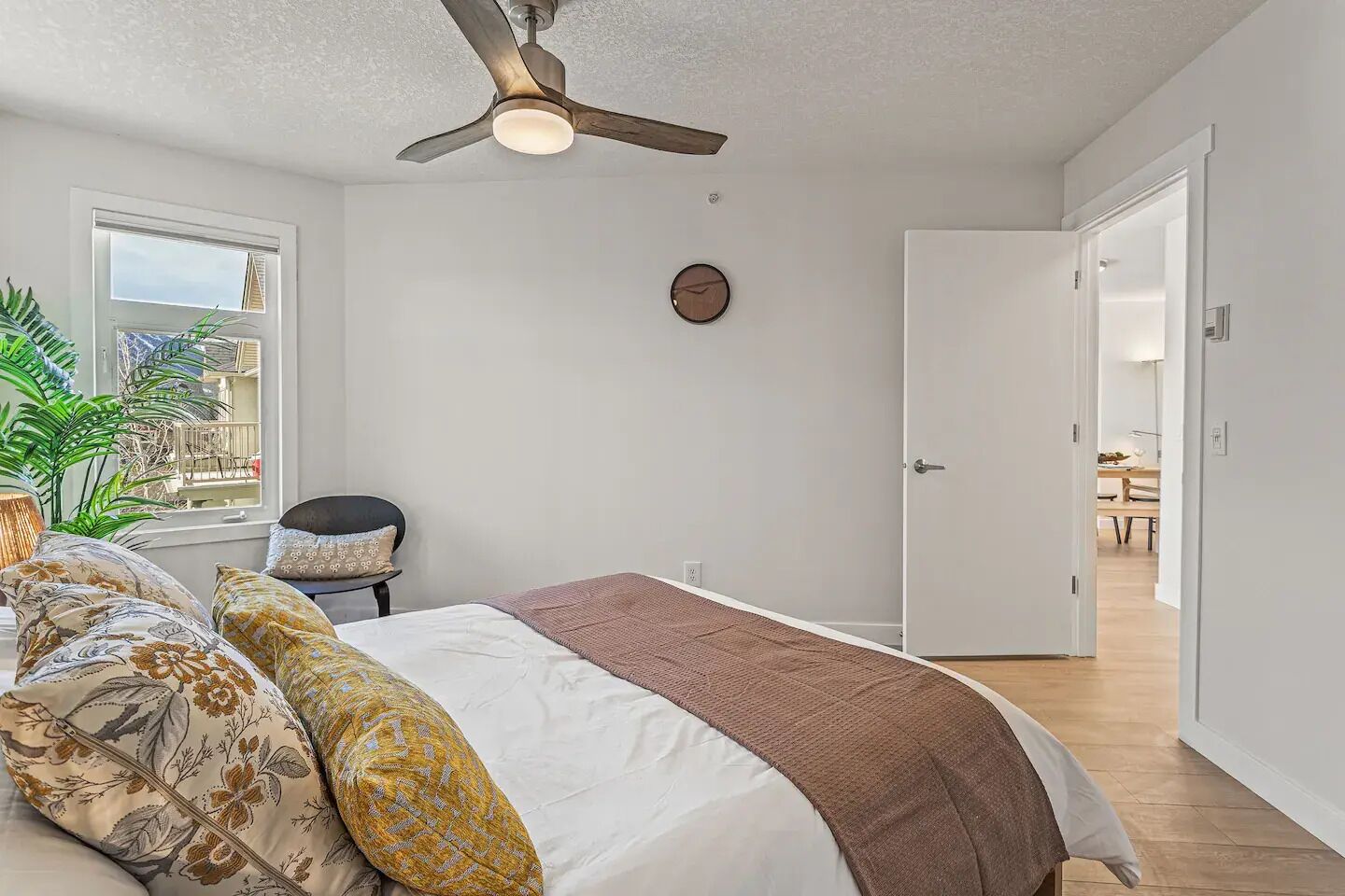 Une chambre à coucher comprenant un lit, un ventilateur de plafond, une fenêtre et une porte donnant sur une autre pièce.