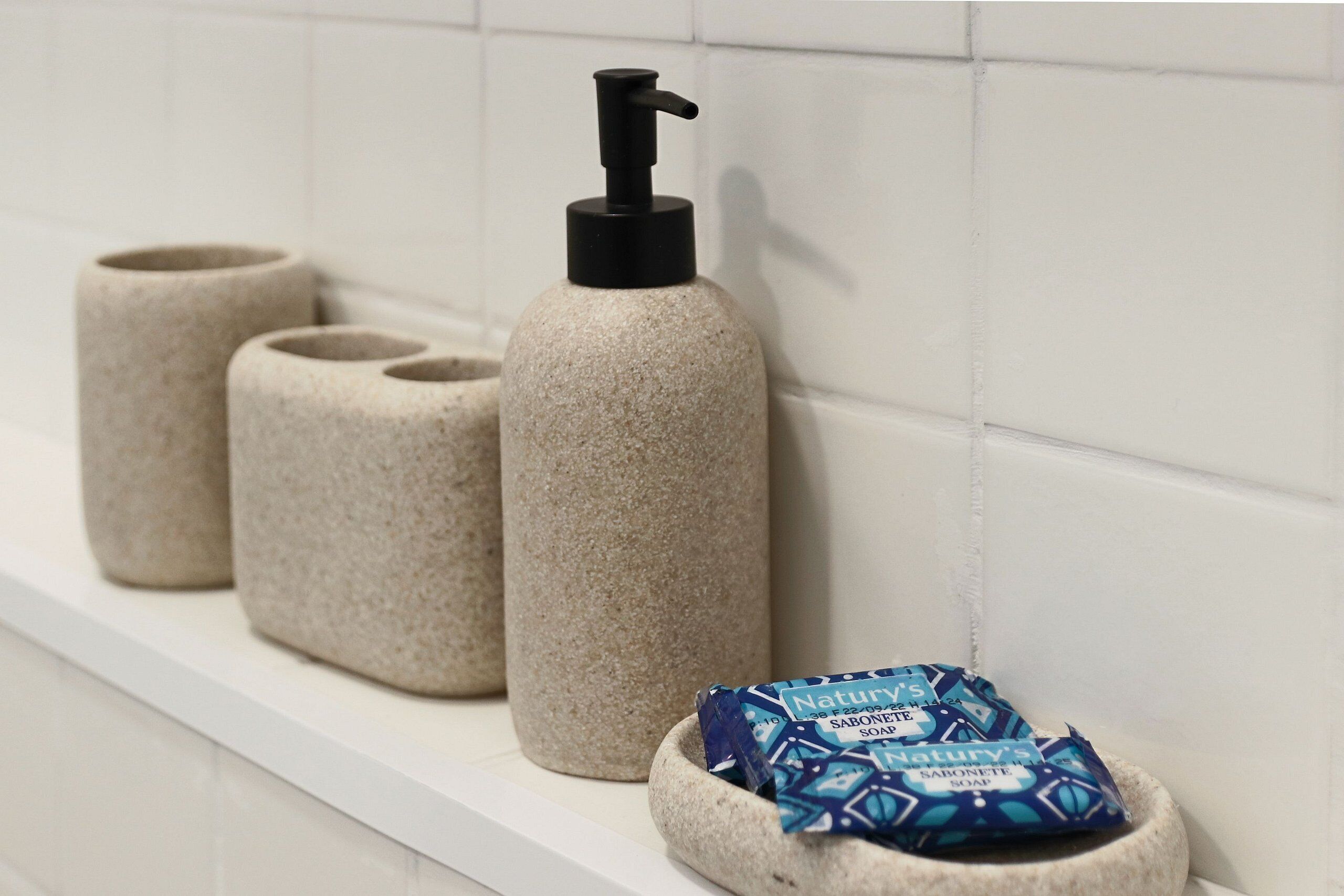 A bathroom shelf with three soap dispensers and a soap bar.
