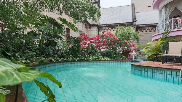 Ein Schwimmbecken, umgeben von üppiger Vegetation und einem Gebäude im klassischen Stil.