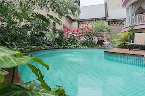 Ein Schwimmbecken, umgeben von üppiger Vegetation und einem Gebäude im klassischen Stil.