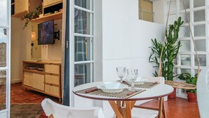 Ein Essbereich mit einem runden Tisch, weißen Stühlen und einem an einem Holzkasten montierten Fernseher.