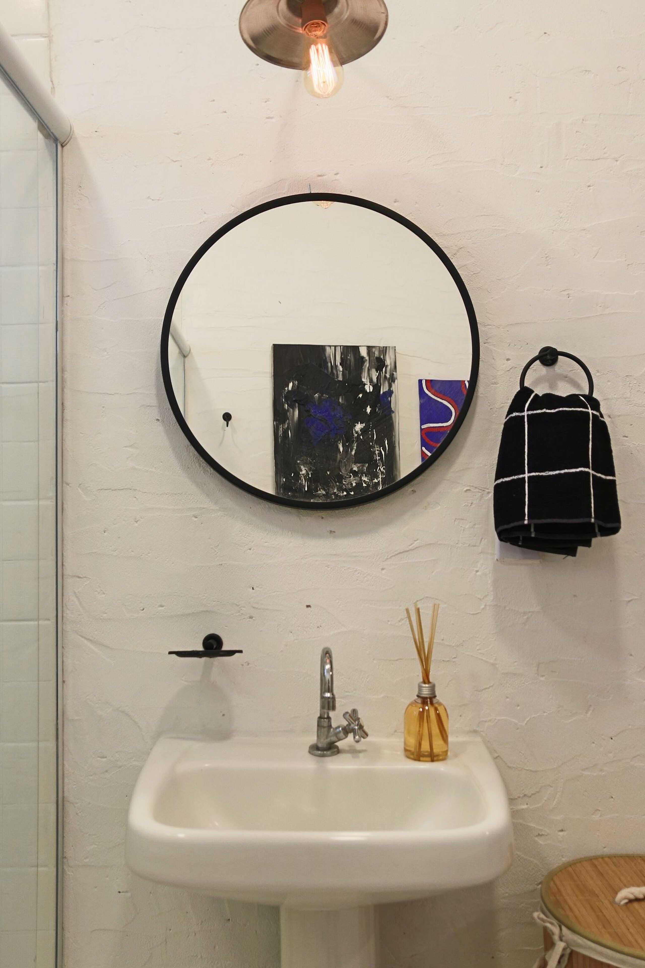 A bathroom with a round mirror, a sink, a hanging towel, and a light fixture.